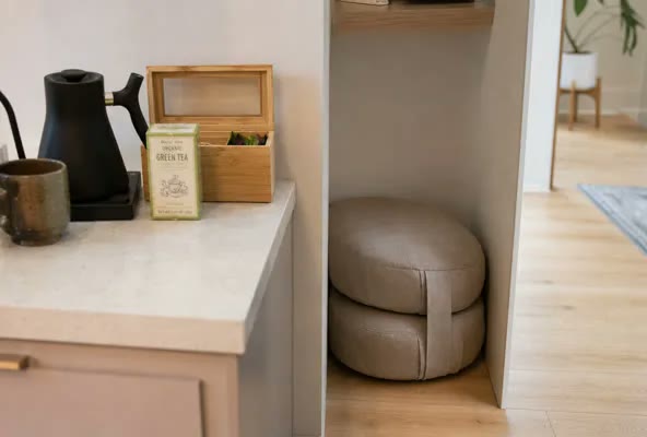 A small folded meditation cushion tucked next to a kitchen tea station, a quiet visual cue