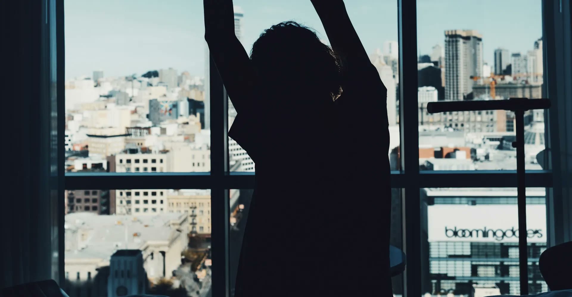 A person stretching in front of a bright window overlooking a city in the morning.