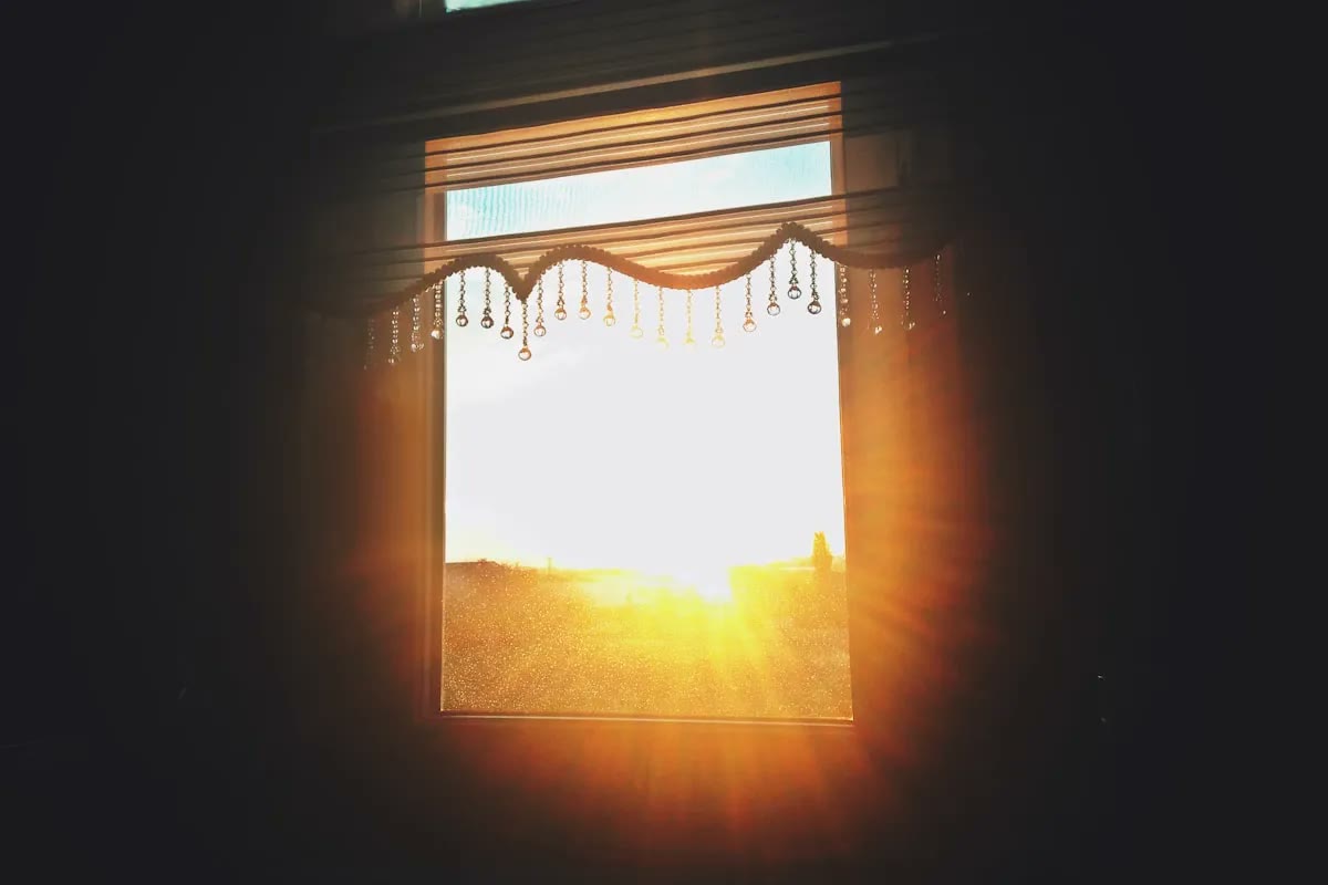 Sunlight streaming through open window blinds into a dim room.