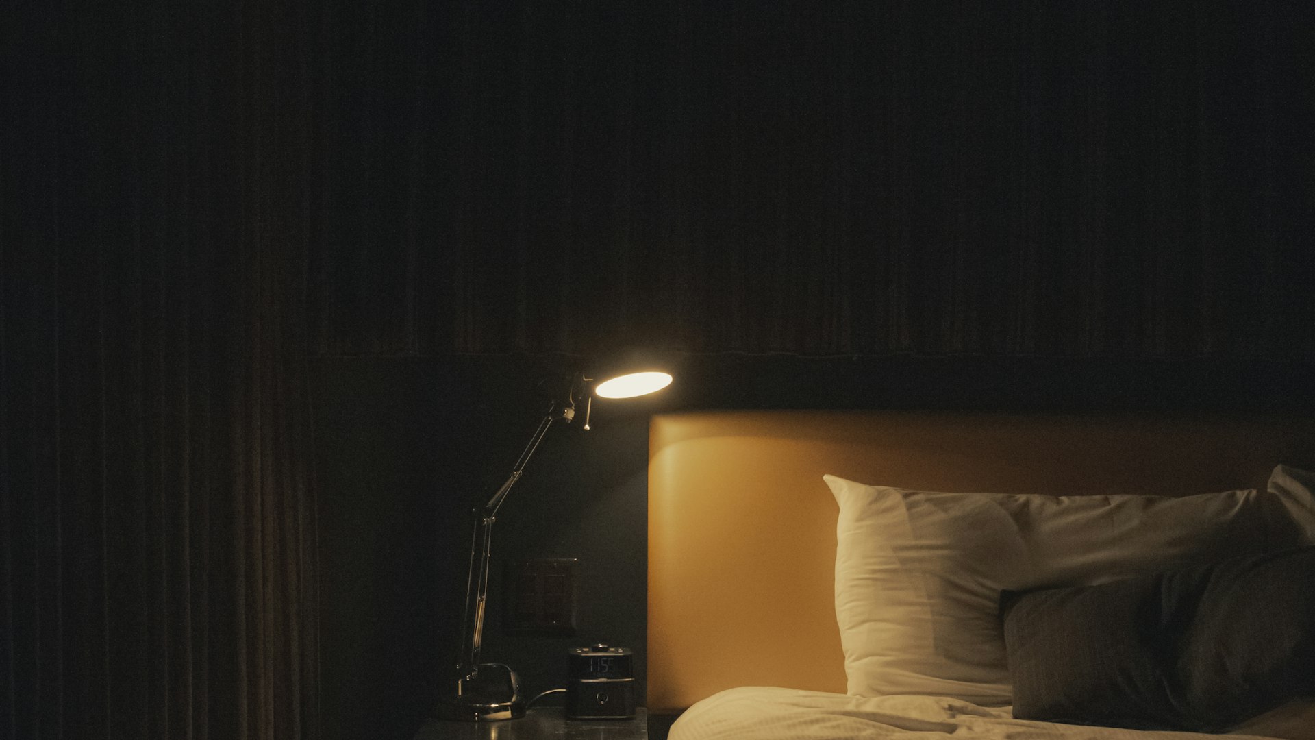 A warm bedside lamp glowing beside a quiet, dimly lit bed at night, setting a calm mood for sleep.
